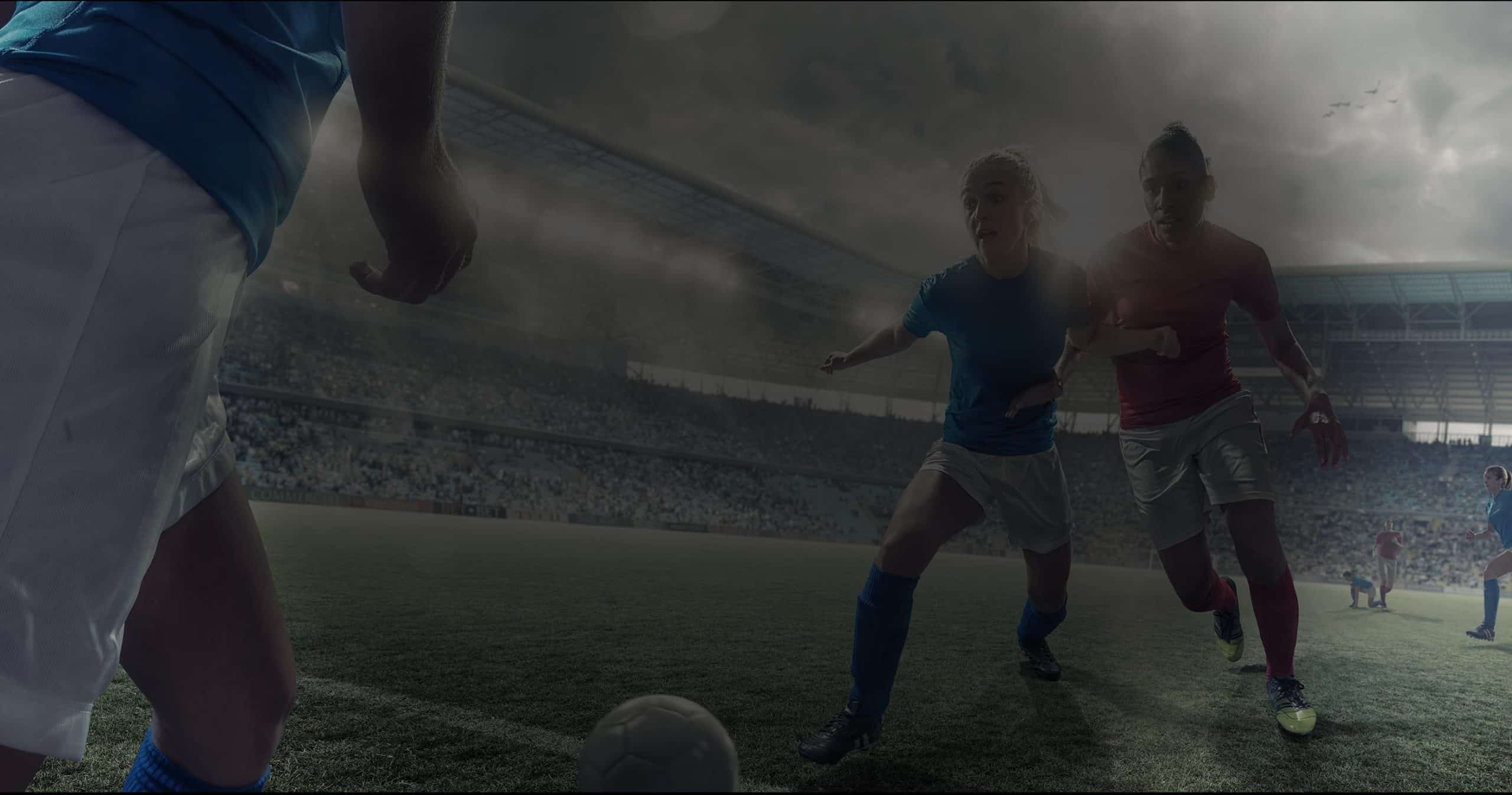 Two soccer players, one in a blue jersey and the other in a red jersey, chase a ball on a professional field with a large crowd in the stands. The scene is dimly lit, highlighting the intensity and action of the game, underscoring the importance of sports nutrition for peak performance.